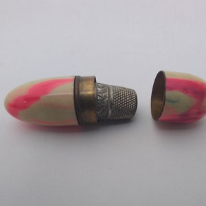 K&ouml;nnte beinhalten: Ein wei&szlig;es und rosafarbenes N&auml;hk&auml;stchen mit einem silbernen Fingerhut darin. Das K&auml;stchen ist ge&ouml;ffnet und der Fingerhut ist sichtbar.