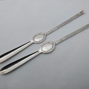 May include: A pair of silver serving forks with ornate handles. The handles have a decorative oval design.