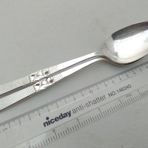 May include: Two silver spoons with an ornate design on the handle. The spoons are laid out on a white surface with a ruler that reads "niceday anti-shatter NO.146340".