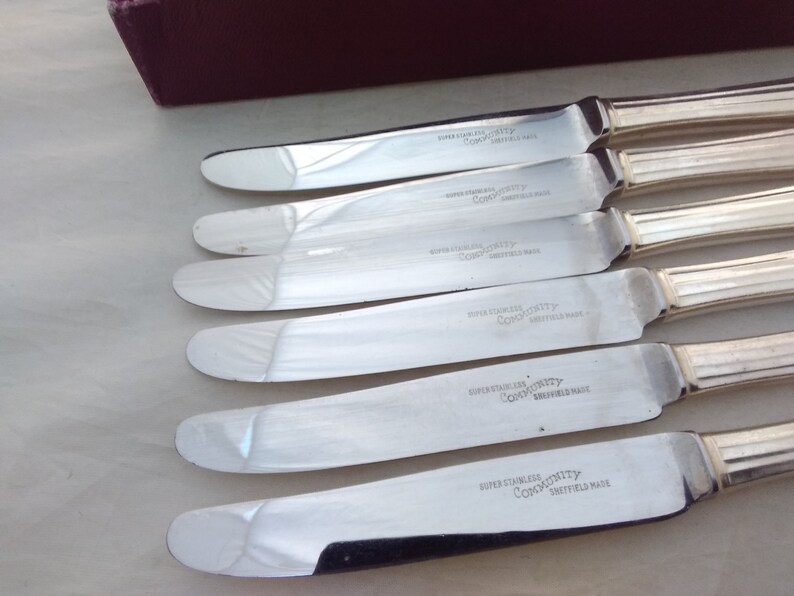 Puede incluir: Cinco cuchillos de mantequilla de plata con mango acanalado y las palabras "Super Stainless Community Sheffield Made" grabadas en la hoja.