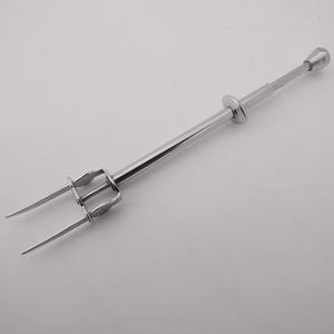 May include: A shiny, silver-colored cake server with a long handle and two prongs. The server has a rounded top and a circular handle grip. The prongs are curved and pointed, designed for serving cakes and pastries.
