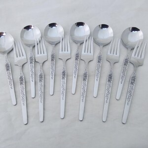 May include: A set of stainless steel silverware, including soup spoons and forks. The silverware has a floral design on the handles. The spoons have a round bowl shape. The forks have three tines.