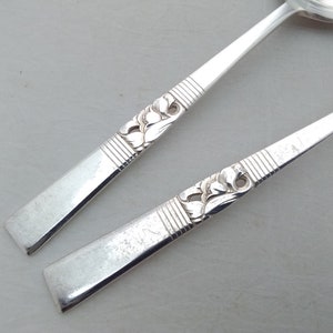 May include: Two silver spoons with ornate floral designs on the handles. The spoons have a rounded bowl shape.