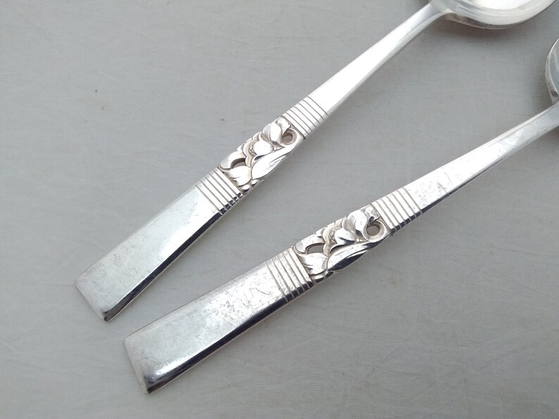 May include: Two silver spoons with ornate floral designs on the handles. The spoons have a rounded bowl shape.