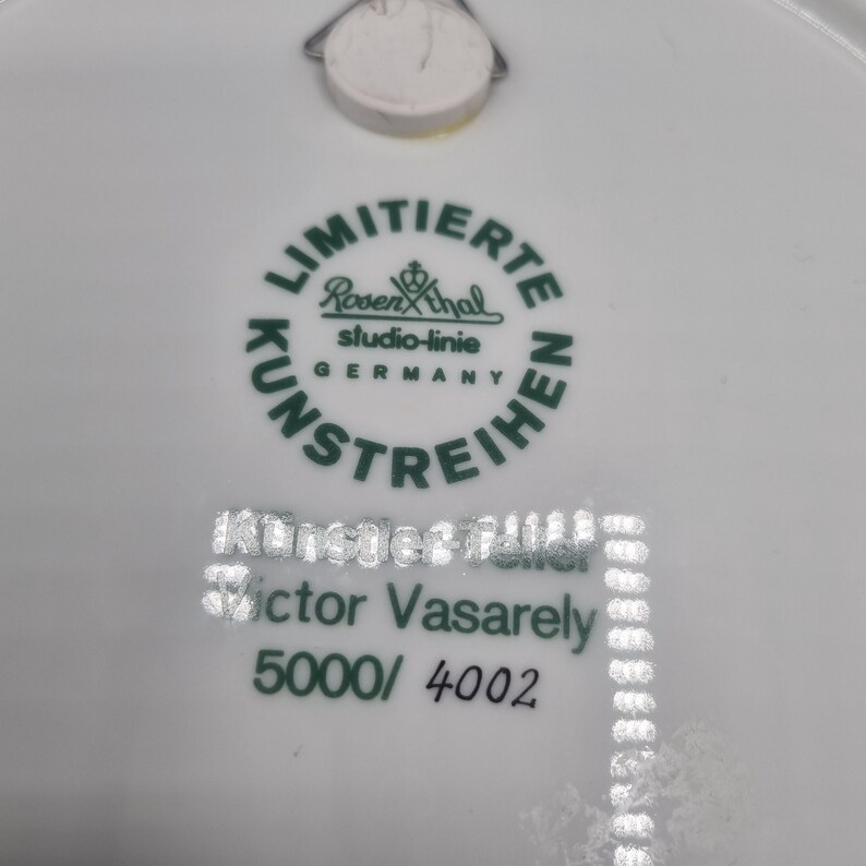 May include: White ceramic plate with green text and a logo. The text includes "LIMITIERTE KUNSTREIHEN" and "Rosenthal studio-linie GERMANY". Below, it reads "K&uuml;nstler Edition Victor Vasarely 5000/4002".