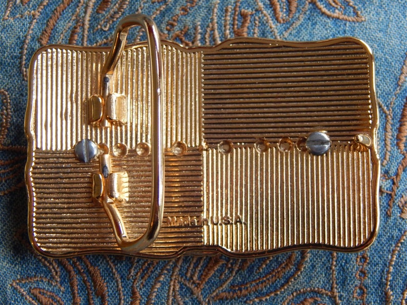 May include: Gold-tone belt buckle with a textured surface and a metal buckle. The buckle has the text "Made in USA" on the back.