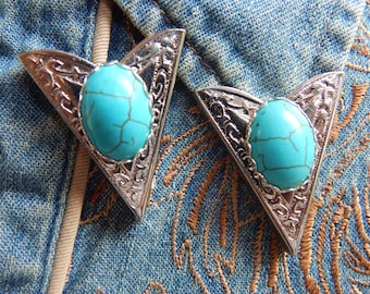 May include: Two silver-toned metal arrowhead-shaped belt buckles with turquoise stones. The buckles have an ornate design.