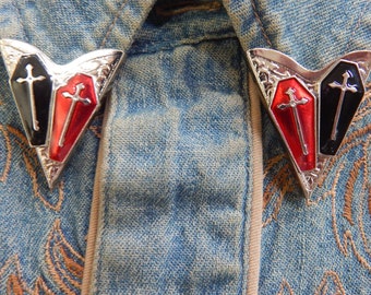 May include: Two silver-toned lapel pins in the shape of a heart with a black and red coffin design. Each coffin has a silver cross on top.