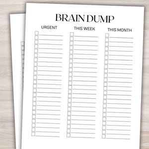 May include: Two white sheets of paper with the words "BRAIN DUMP" at the top. The sheets are divided into columns labeled "URGENT", "THIS WEEK", and "THIS MONTH", with rows of checkboxes for each category. The paper is on a light wood surface.
