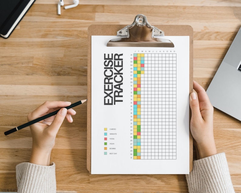 May include: A white paper exercise tracker sheet held on a brown clipboard. The document features the text EXERCISE TRACKER, a grid with numbered rows from 01 to 30, and a color-coded legend for cardio, weights, yoga, aqua, boxing, and rest day.