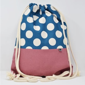 Könnte beinhalten: Eine blaue und rosafarbene Kordeltasche mit weißen Punkten. Die Tasche hat eine weiße Kordel und ein kleines Etikett am Boden.