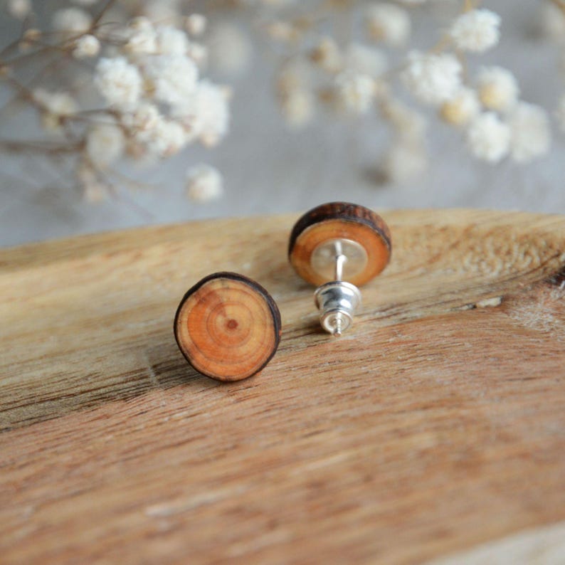 May include: A pair of wooden earrings with a natural wood grain pattern. The earrings are round and have a silver post.