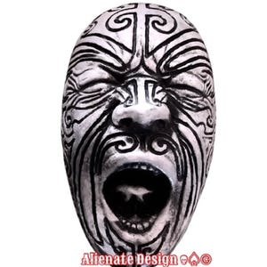 Peut inclure: Un masque argenté avec des motifs tribaux noirs et une bouche ouverte. Le masque a les yeux fermés et des motifs complexes. Le texte "Alienate Design" est visible en bas.