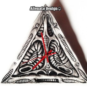 May include: A triangular wall clock with a black and white alien face design. The clock has red hands and a white background.