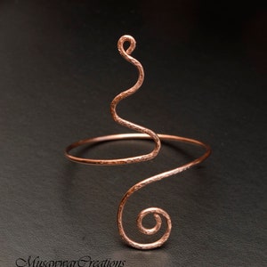 May include: A hammered copper wire bracelet with a unique, swirling design. The bracelet is open and adjustable to fit most wrists.