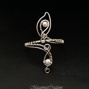 May include: A silver wire ring with two white pearls. The ring is designed in a swirling, abstract pattern.