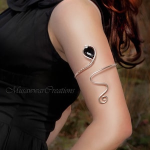 May include: A silver wire arm cuff with a black gemstone and a clear rhinestone. The cuff is shaped like a snake and has a spiral design at the end.
