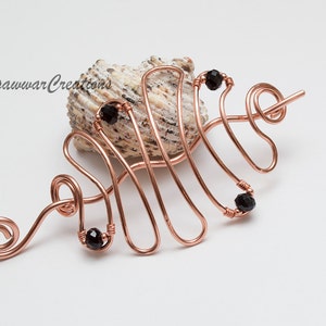 Puede incluir: Un peine para el cabello de alambre de cobre con cuentas negras. El peine tiene forma de onda y tiene una espiral en el extremo.