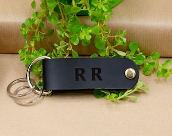 Könnte beinhalten: Schwarzer Leder-Schlüsselanhänger mit einem silbernen Schlüsselring und den Initialen "RR" in weiß geprägt.