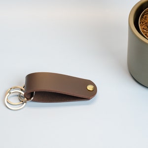 May include: A brown leather key chain with a brass button and two silver key rings.