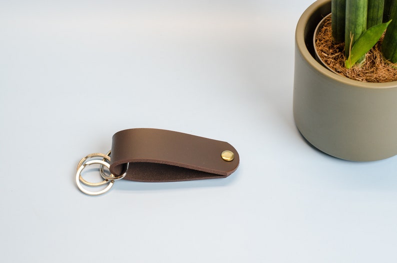 May include: A brown leather key chain with a brass button and two silver key rings.