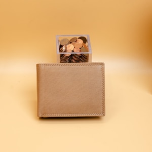 May include: A brown leather wallet with a stitched edge. The wallet is sitting on a light brown surface.
