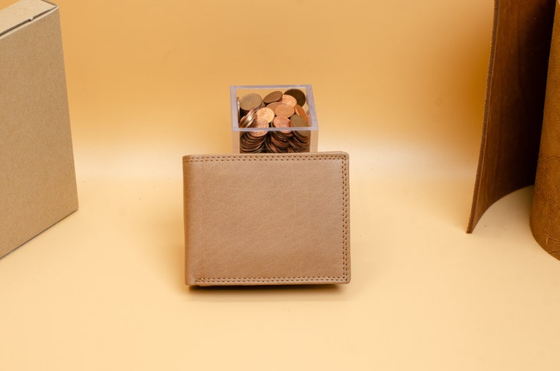 May include: A brown leather wallet with a stitched edge. The wallet is sitting on a light brown surface.