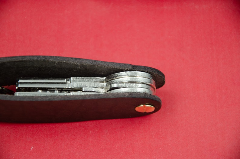 May include: A black leather key holder with a brass screw and multiple keys inside.