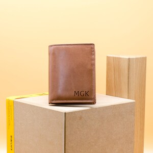 May include: A brown leather wallet with the initials "MGK" embossed on the front.