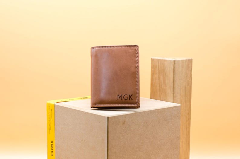 May include: A brown leather wallet with the initials "MGK" embossed on the front.