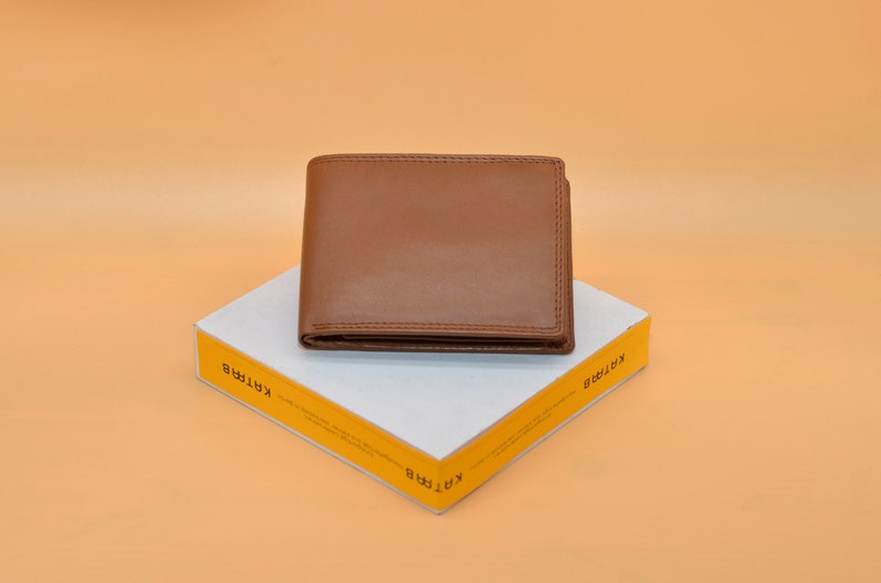 May include: A brown leather wallet on a white box with yellow text that says "KARTIRA" on both sides.
