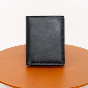 May include: A black leather wallet with a smooth, textured surface. The wallet is closed and sitting on a brown surface.