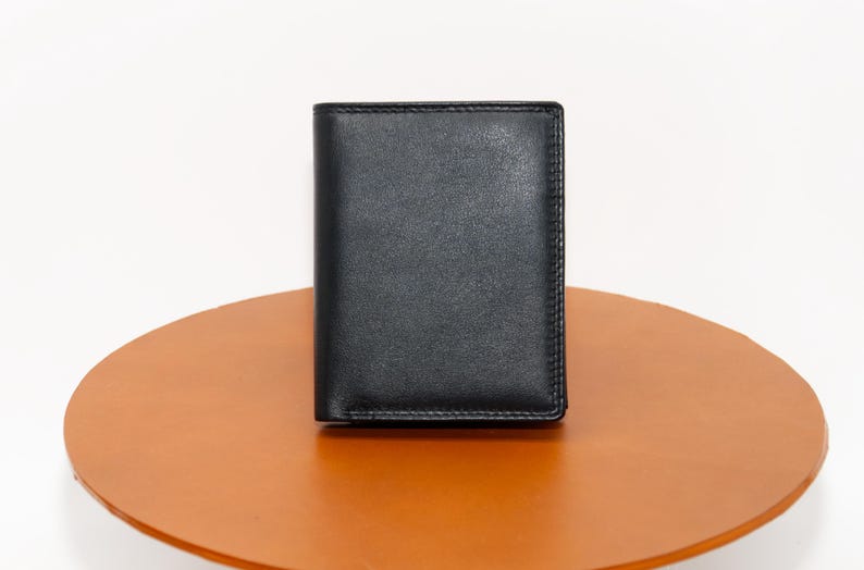 May include: A black leather wallet with a smooth, textured surface. The wallet is closed and sitting on a brown surface.