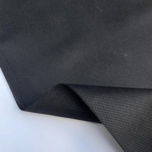 Könnte beinhalten: Schwarzer Stoff mit einem strukturierten, gewebten Muster. Der Stoff ist in der Mitte gefaltet und zeigt die Unterseite.