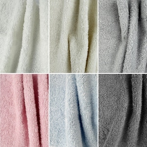 May include: A collage of six soft, textured towels in various colors. The colors include white, cream, gray, pink, light blue, and dark gray. The towels appear to be made of a plush material, with visible fibers and folds.