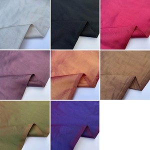 Op de afbeelding: Een verzameling stofstalen in verschillende kleuren, waaronder wit, zwart, bordeauxrood, oranje, bruin, groen en blauw. De stof heeft een subtiele glans en een gladde textuur.