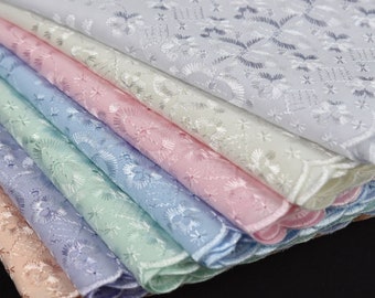 May include: A stack of eight embroidered handkerchiefs in various pastel colors, including white, light pink, light blue, and light green. The handkerchiefs are folded and arranged in a fan shape, with the white handkerchief on top.