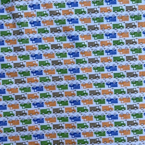 May include: A white fabric with a repeating pattern of small trucks in blue, green, orange, and brown. The trucks are facing right and have a simple design.