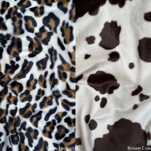 May include: Close-up of two fabric swatches. The left swatch is a white fabric with a brown and black snow leopard print. The right swatch is a white fabric with a brown cow print.