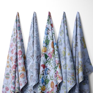 Op de afbeelding: Vier blauwe theedoeken met verschillende paasmotieven. De patronen omvatten konijnen, eieren, bloemen en kabouters.