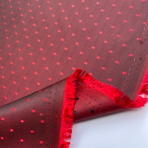 May include: A close-up shot of burgundy fabric featuring a polka dot pattern in red. The fabric has a fringed edge in red. The material is sheer and lightweight, ideal for clothing or decorative purposes.
