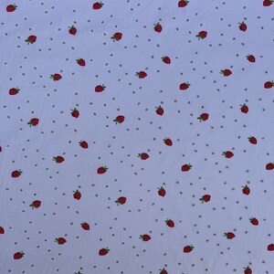 Könnte beinhalten: Ein hellblauer Stoff mit einem sich wiederholenden Muster aus kleinen roten Erdbeeren. Die Erdbeeren sind zufällig über den Stoff verteilt.