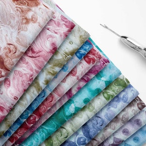 Può includere: Un mucchio di dieci quadrati di tessuto con un motivo marmoreo in vari colori, tra cui rosa, blu, verde e marrone. Il tessuto è piegato a ventaglio, con il quadrato superiore piegato sugli altri.