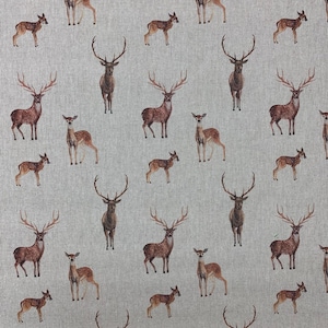 Op de afbeelding: Een stof met een herhalend patroon van herten in verschillende maten en poses. De herten zijn afgebeeld in bruin- en beigetinten, met gedetailleerde geweien op de bokken. De achtergrond is lichtgrijs.