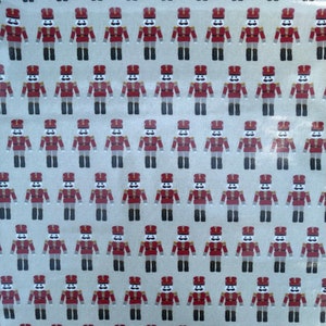 Peut inclure: Un motif répété de soldats de jouet illustrés sur un tissu beige. Les soldats portent des uniformes rouges et dorés avec des chapeaux noirs et des visages blancs.