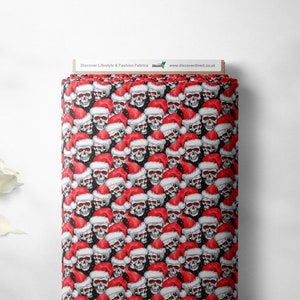 May include: Black fabric with a repeating pattern of white skulls wearing red Santa hats. The fabric has a white snowflake pattern.