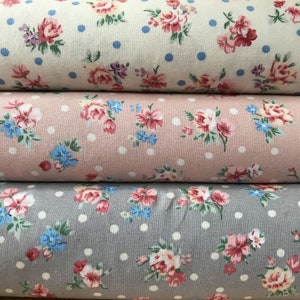Peut inclure: Trois rouleaux de tissu à imprimé floral et à pois blancs. Le rouleau du haut est crème avec des pois bleus, le rouleau du milieu est rose avec des pois blancs et le rouleau du bas est gris avec des pois blancs.