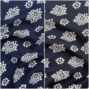 May include: Two fabric samples, side-by-side, featuring a repeating pattern of white floral designs on a navy blue background. The flowers vary in size and are scattered across the fabric, creating a visually appealing textile.