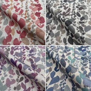 Op de afbeelding: Vier stofstalen met een witte achtergrond en een herhalend patroon van gestileerde bladeren in verschillende kleuren. De stalen zijn gerangschikt in een raster, met de linkerbovenste staal met rode en oranje bladeren, de rechterbovenste staal met grijze bladeren, de linkeronderste staal met paarse bladeren en de rechteronderste staal met blauwe bladeren.