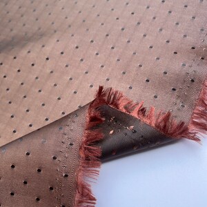 May include: A close-up shot of a brown fabric with a dotted pattern. The fabric has a textured surface and a frayed edge. The dots are evenly spaced and dark in colour. The fabric is folded over, revealing a darker underside.
